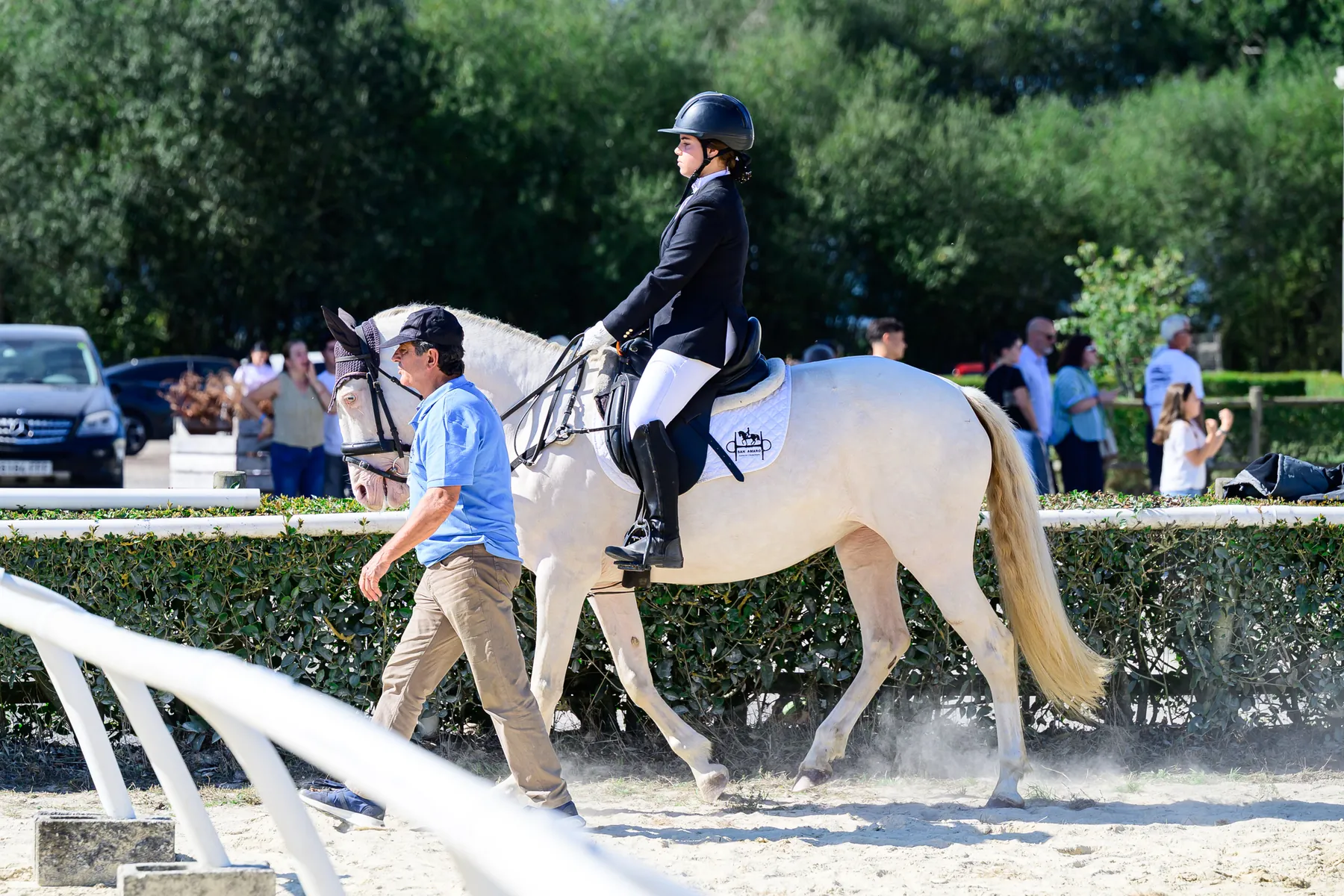 Joven amazona en un poni tordo, acompañada a pie durante un concurso