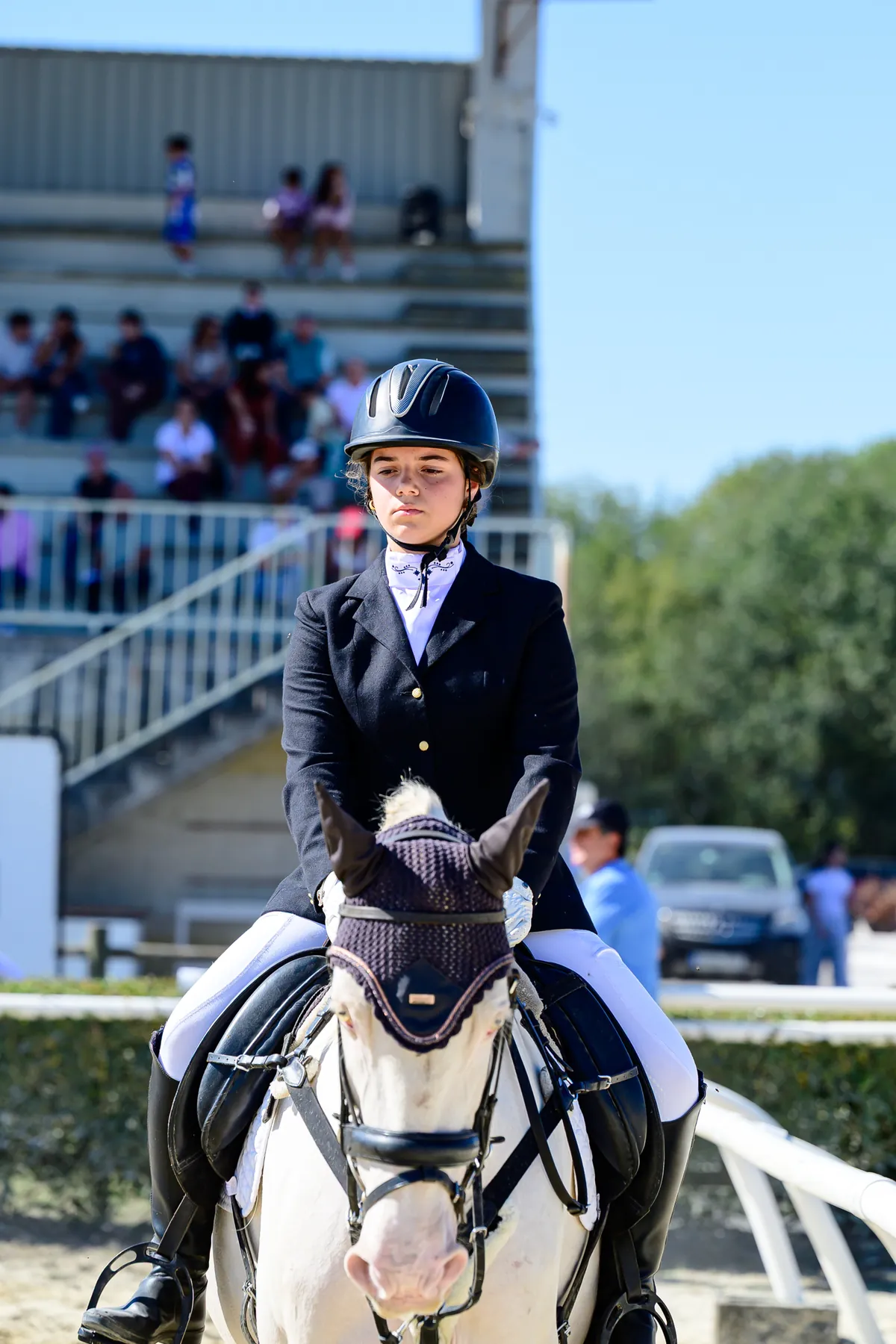 Joven amazona con casco montando un poni tordo en un concurso