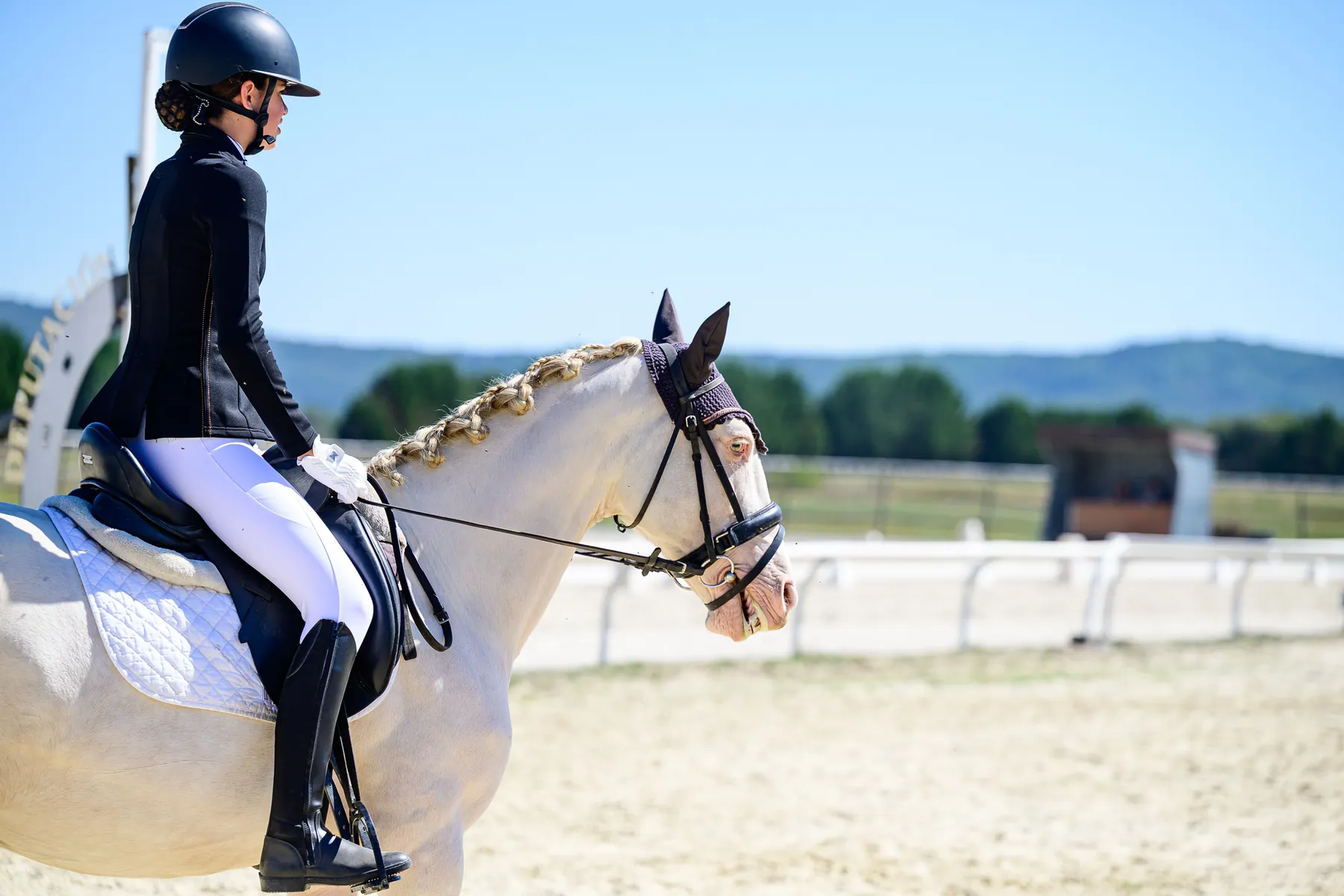 Joven amazona montando un poni tordo en la pista de concurso